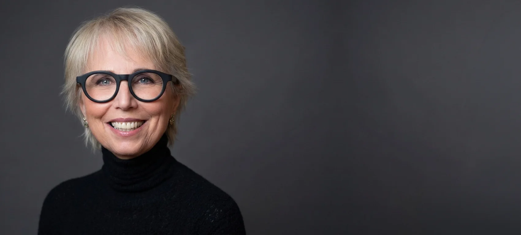 Geneen Roth smiling, in round dark glasses and a black turtleneck